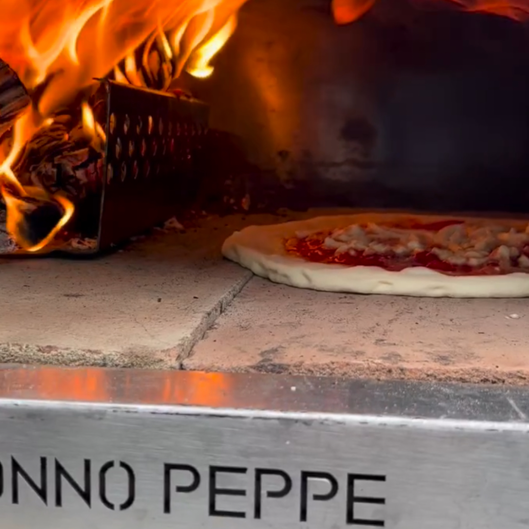 Bilden fångar ögonblicket när en napolitansk pizza gräddas perfekt i en Nonno Peppe pizzaugn. Med en autentisk napolitansk receptur och traditionella ingredienser tillagas pizzan till perfektion i den vedeldade ugnen. Nonno Peppe strålar med sitt klassiska italienska snitt och rostfria ytterhölje, medan den 40 mm äkta biscotti-baksten ger den perfekta grundstrukturen för en krispig botten. Den generösa 60x60 cm bakyta erbjuder gott om plats för att skapa den perfekta pizzan med generösa toppingar och en lockande doft. Med en Nonno Peppe pizzaugn får varje pizzabagare en känsla av äkthet och tradition med varje tugga av den läckra napolitanska pizzan.